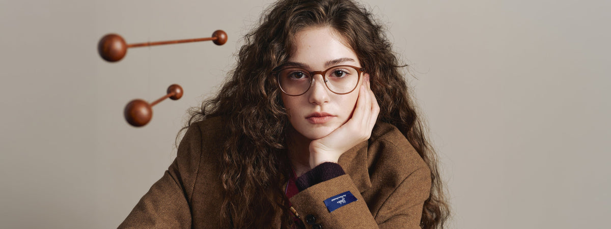 Model wearing CARIN glasses against a warm grey wall