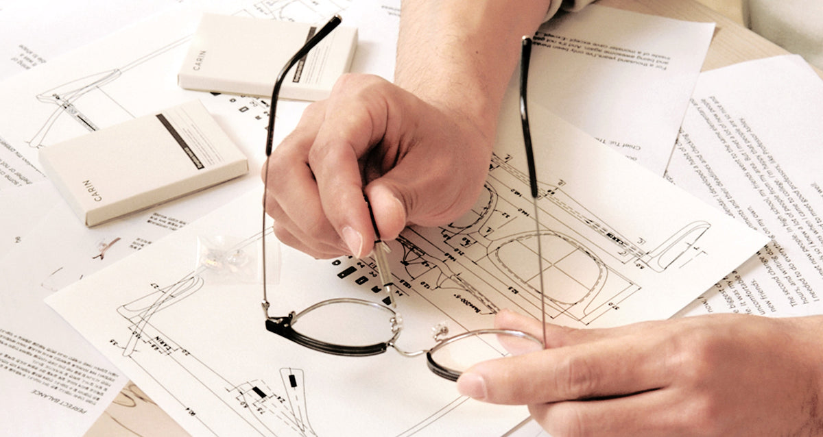 Hands adjusting a CARIN frame over design sketches