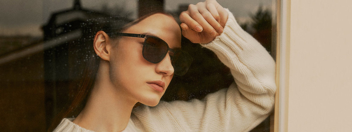 Woman in VYCOZ sunglasses at a rain-streaked window