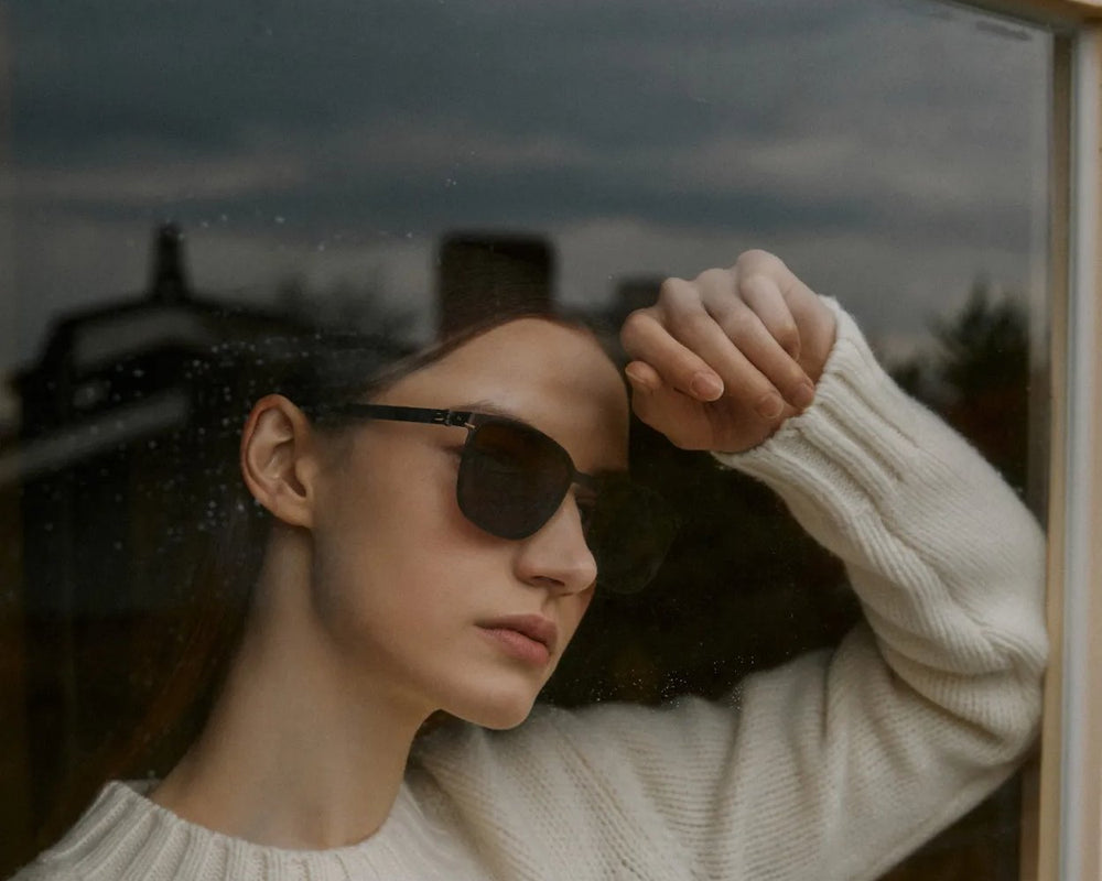 Woman in VYCOZ sunglasses at a rain-streaked window
